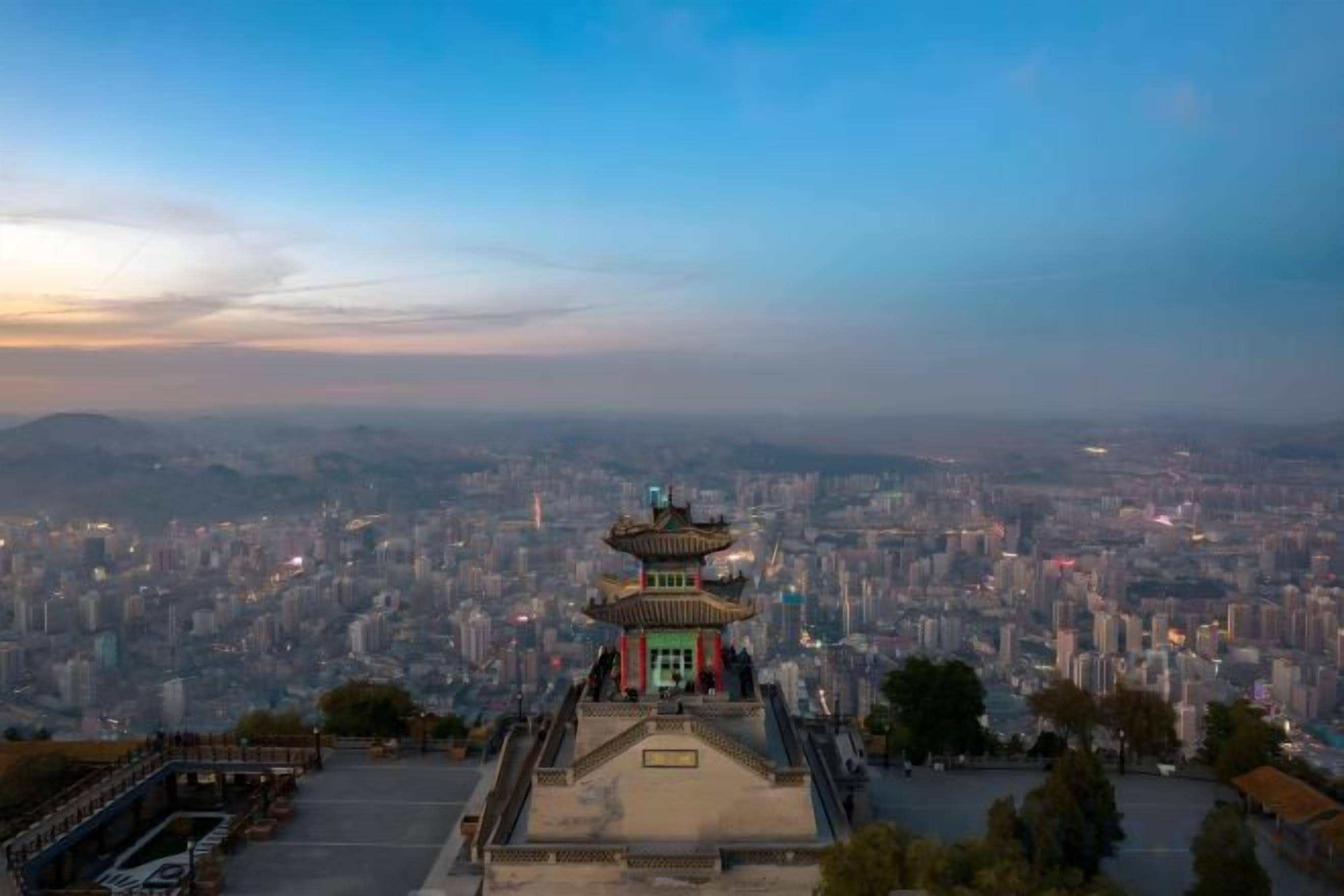 A pagoda-style building with a traditional architectural design, surrounded by a cityscape with numerous buildings and a clear sky.