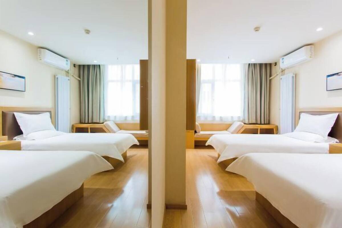 A hotel room with two beds, a wooden floor, and a large window with curtains.