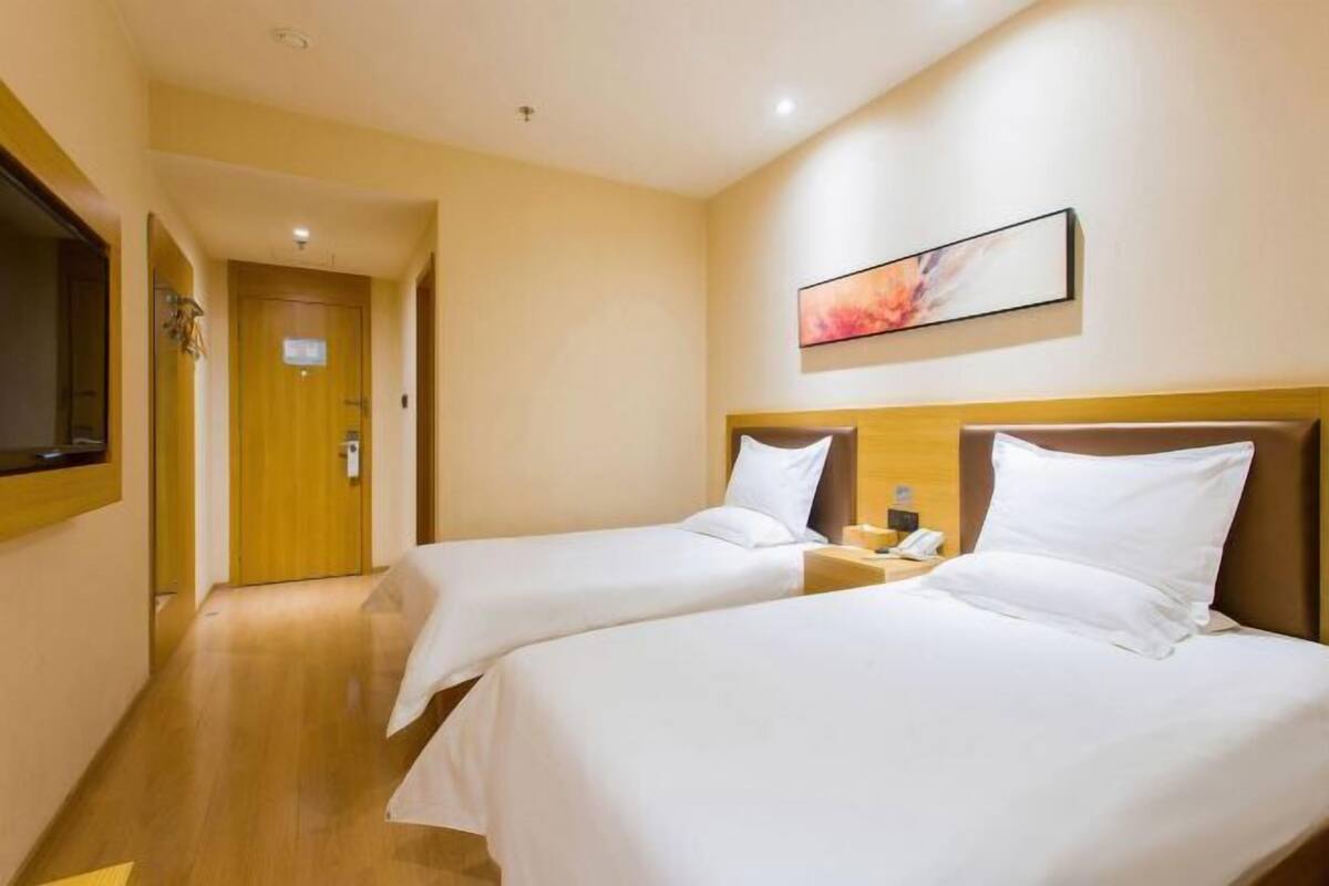 A hotel room with two beds, a wooden headboard, a bedside table with a lamp, and a painting on the wall.