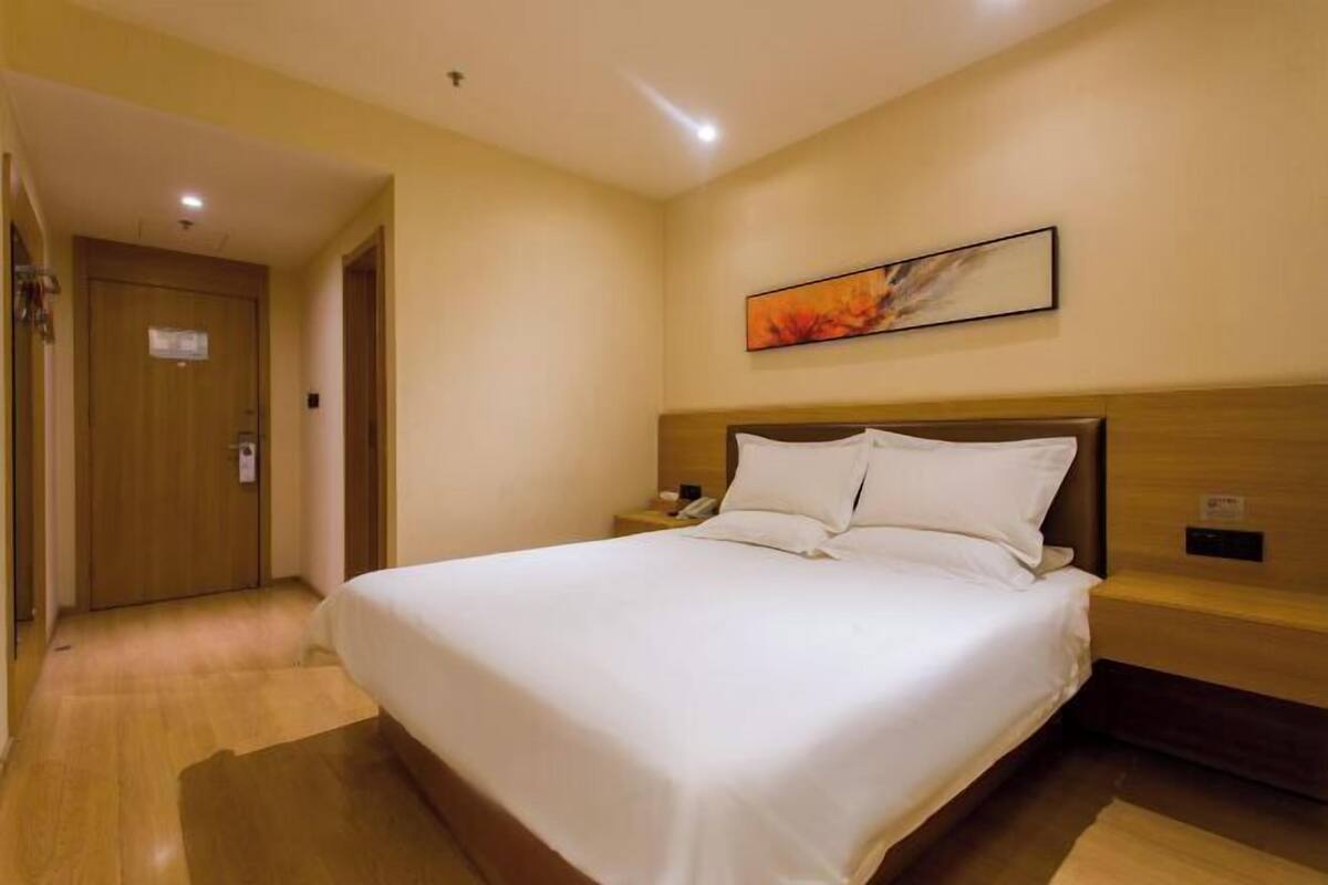 A hotel room with a large bed, wooden headboard, a nightstand, a painting on the wall, and a wooden door.