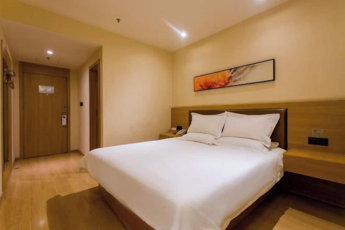 A hotel room with a large bed, wooden headboard, a nightstand, a painting on the wall, and a wooden door.