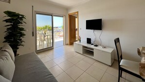 Ein modernes Wohnzimmer mit einer Couch, einem Fernseher, einem Essbereich mit Stühlen und einem großen Fenster mit Blick auf die Stadt.