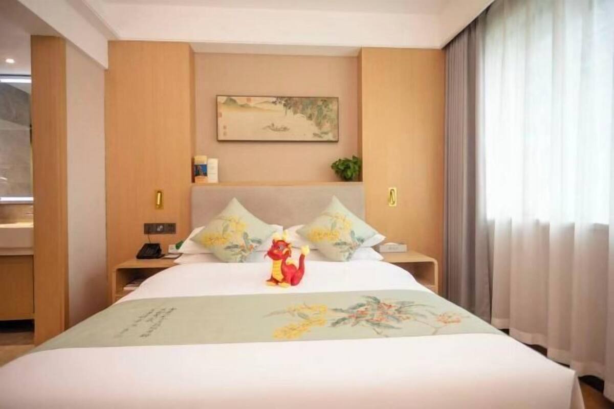 A hotel room with a bed, a nightstand, a wall-mounted painting, and a window with curtains.