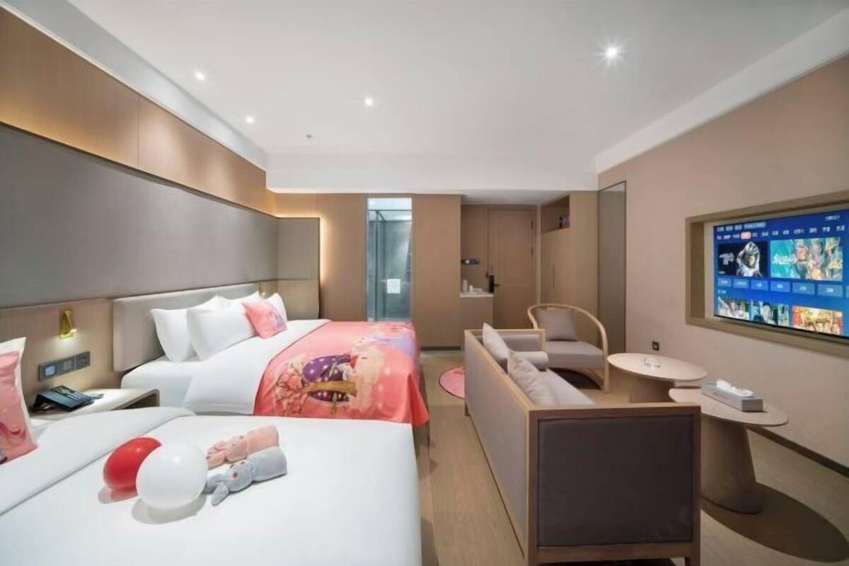 A modern hotel room with a bed, a seating area, a TV, and a small table.