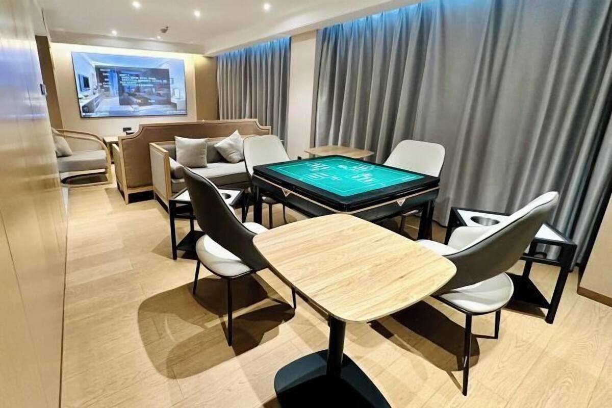 A modern hotel room with a pool table, comfortable seating, and a large screen displaying a cityscape.