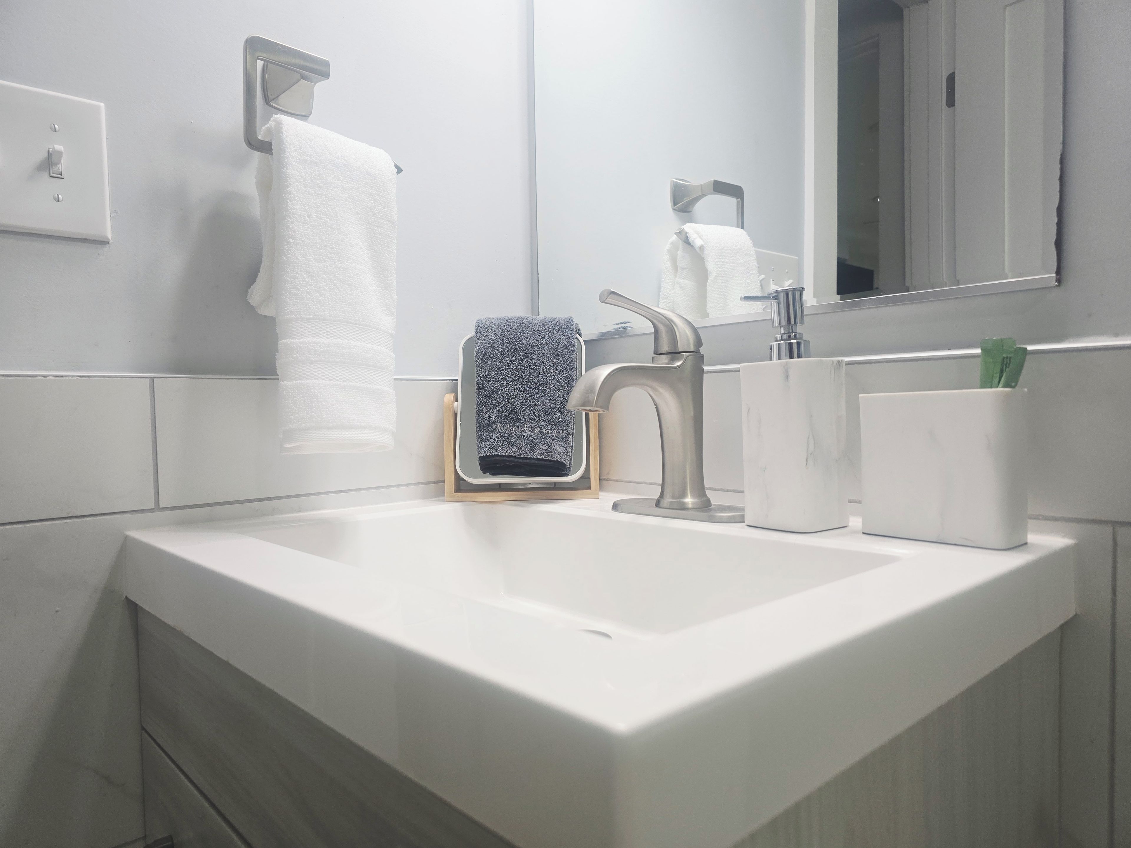 Un baño con lavamanos blanco, toallero, espejo y dispensador de jabón.