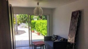 A modern room with a large sliding glass door leading to a patio, a sofa with cushions, a small table with a bench, and a large abstract painting on the wall.