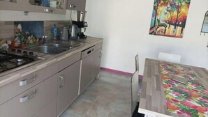 A kitchen with a gas stove, sink, and a coffee maker. There is a dining table with chairs and a colorful painting on the wall.