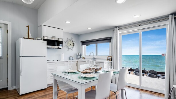 A modern kitchen with white cabinetry, a built-in oven, and a large window overlooking the sea.