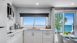 A modern kitchen with white cabinetry, a built-in oven, and a window overlooking the sea.
