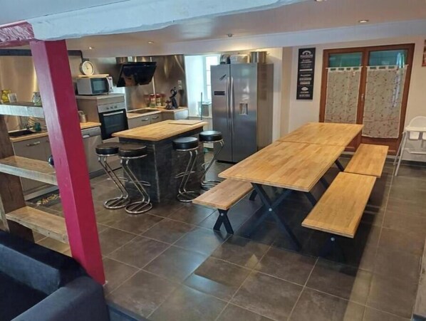 A modern kitchen with a wooden table and bar stools, a refrigerator, and a microwave.