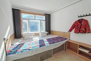 A single-bed room with a window, a bed with a colorful quilt, a wooden headboard, a bench, and a coat rack with a jacket. - Wuchang Snow Valley Jiaxin Inn (Wuchang)