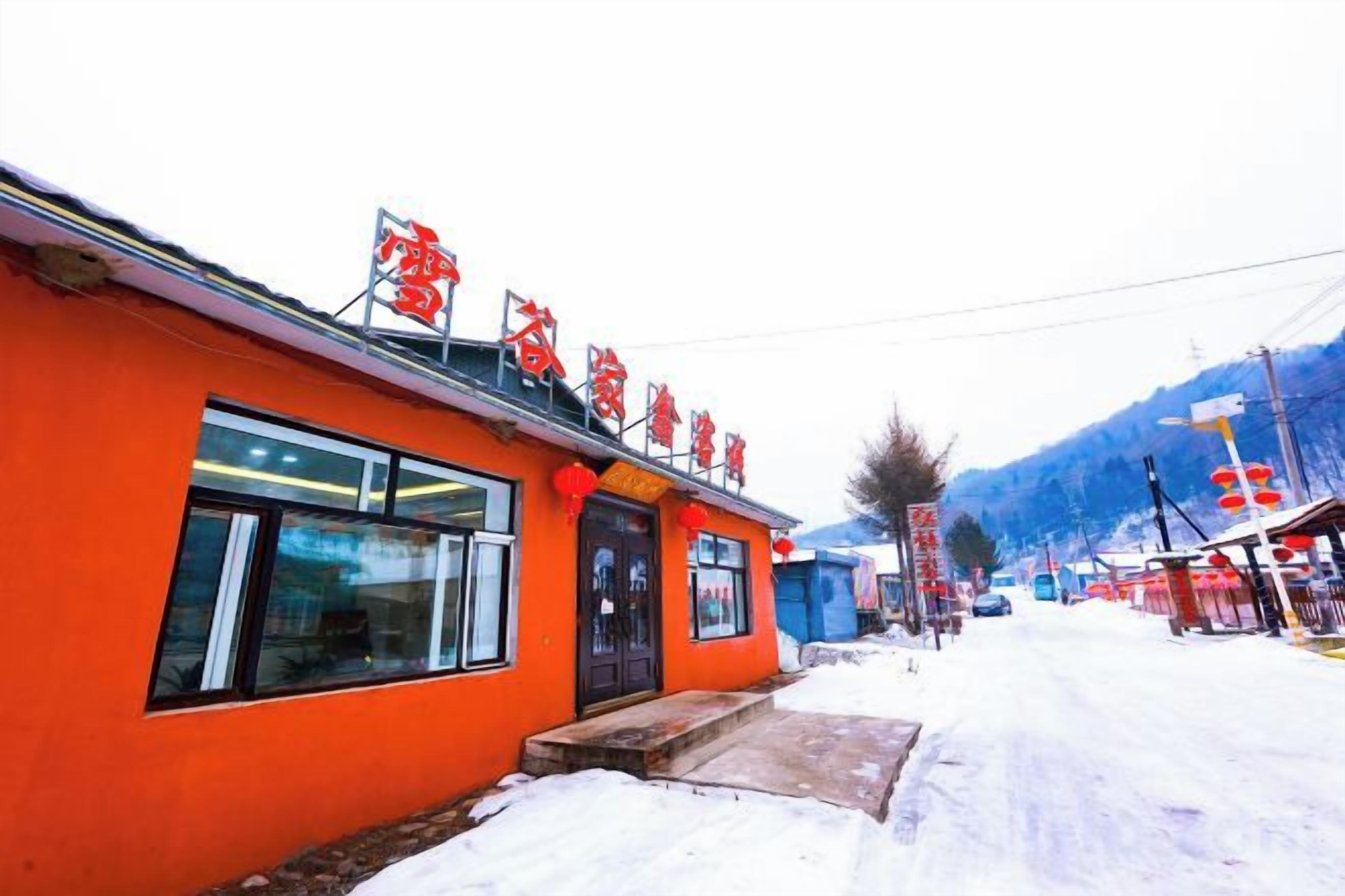 A building with a red facade and signage, a snow-covered street, and a mountainous backdrop.