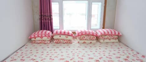 A bedroom with a floral-patterned bedspread, a window with curtains, and a view of the outside.