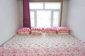 Un dormitorio con una colcha estampada con motivos florales, una ventana con cortinas y vistas al exterior.