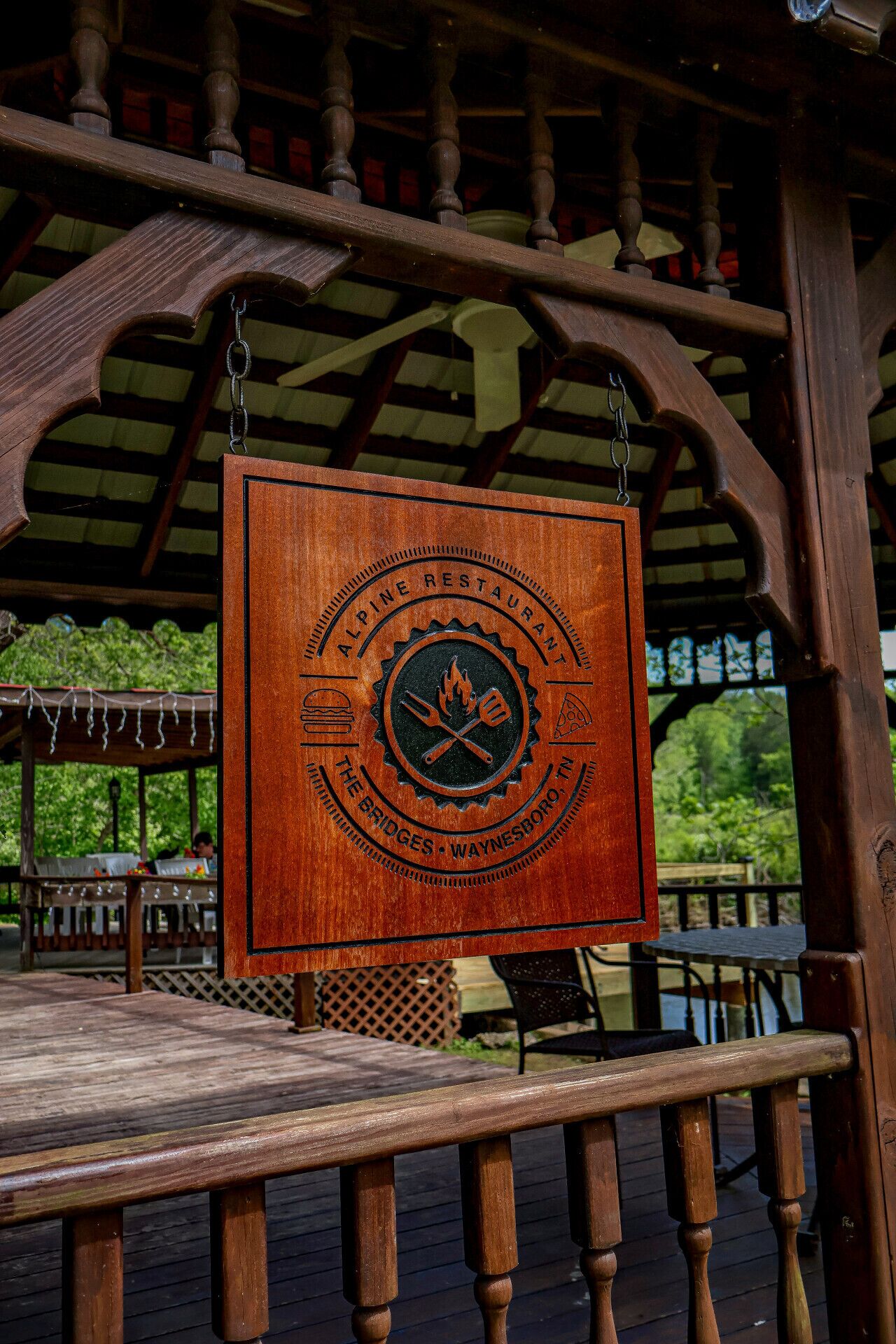 A wooden sign with the text "Alpine Restaurant" and "The Bridges - Waynesboro, TN" hanging from a wooden structure.