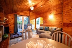 A cozy cabin interior with wooden walls, a sofa, a dining table, and a fireplace. - Cozy Log Cabin 346 - Rural Mid Wales (Blaenau Ffestiniog)