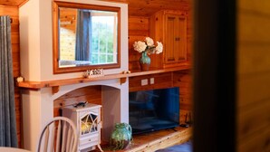 Ein Holzblockhaus-Interieur mit Kamin, einem Spiegel darüber und einem kleinen Tisch mit Blumen.
