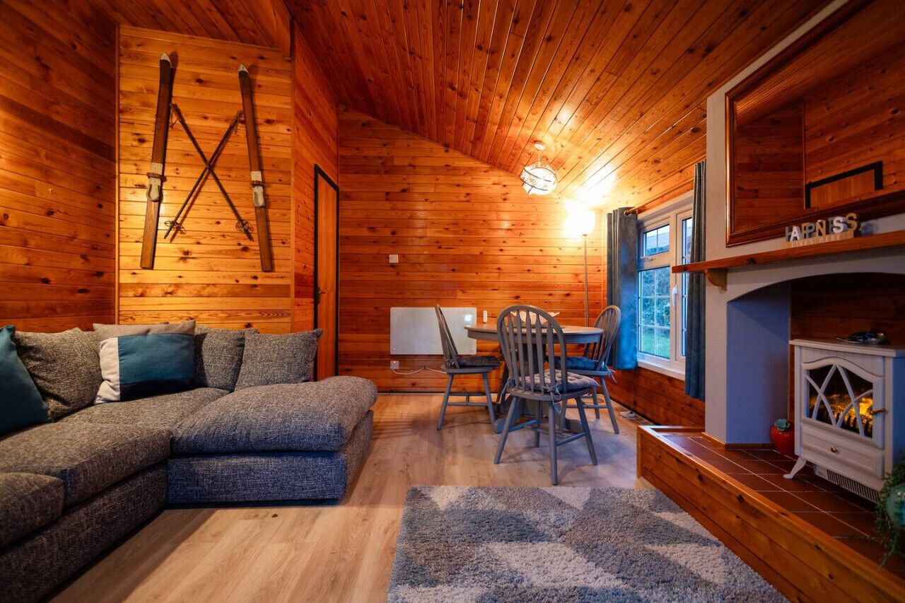 A cozy cabin interior with a wooden ceiling, a fireplace, a dining area, and a large couch.