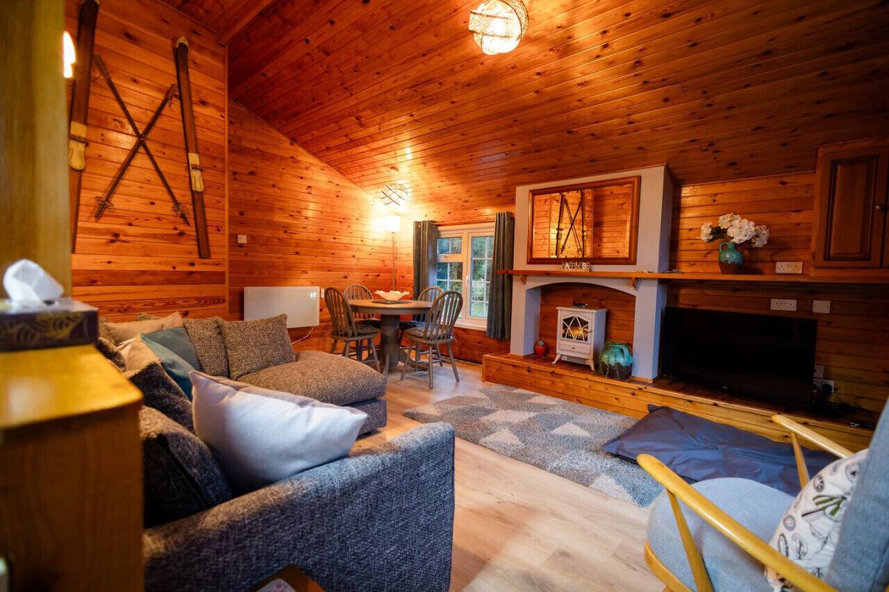 A cozy wooden cabin interior with a fireplace, wooden walls, and a dining area.