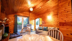 Ein gemütliches Blockhaus-Interieur mit Holzwänden, einem Esstisch mit Glasdeko, einer Couch und einem Sessel.