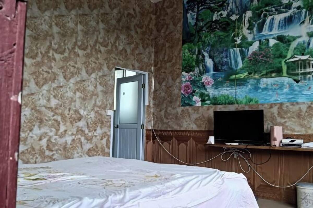 A bedroom with a bed, a TV on a wooden shelf, and a mural of a waterfall.