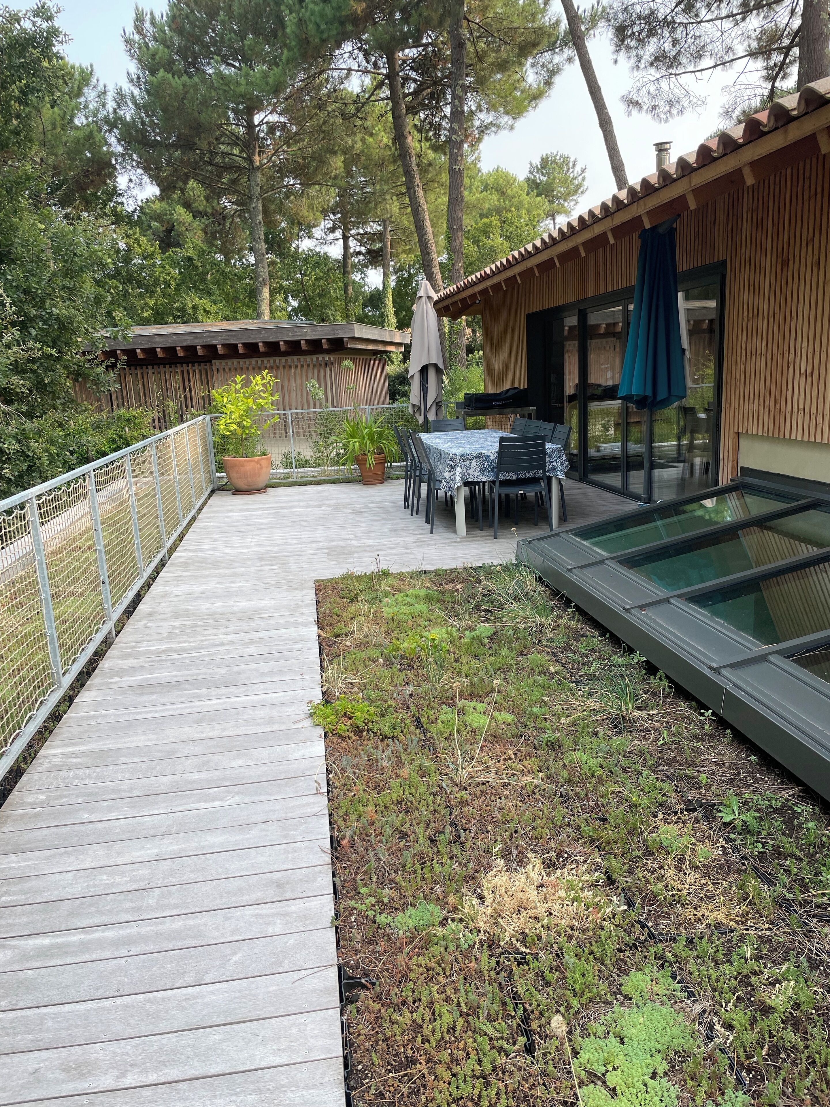 A wooden deck with a table and chairs, surrounded by a wooden fence and potted plants.
