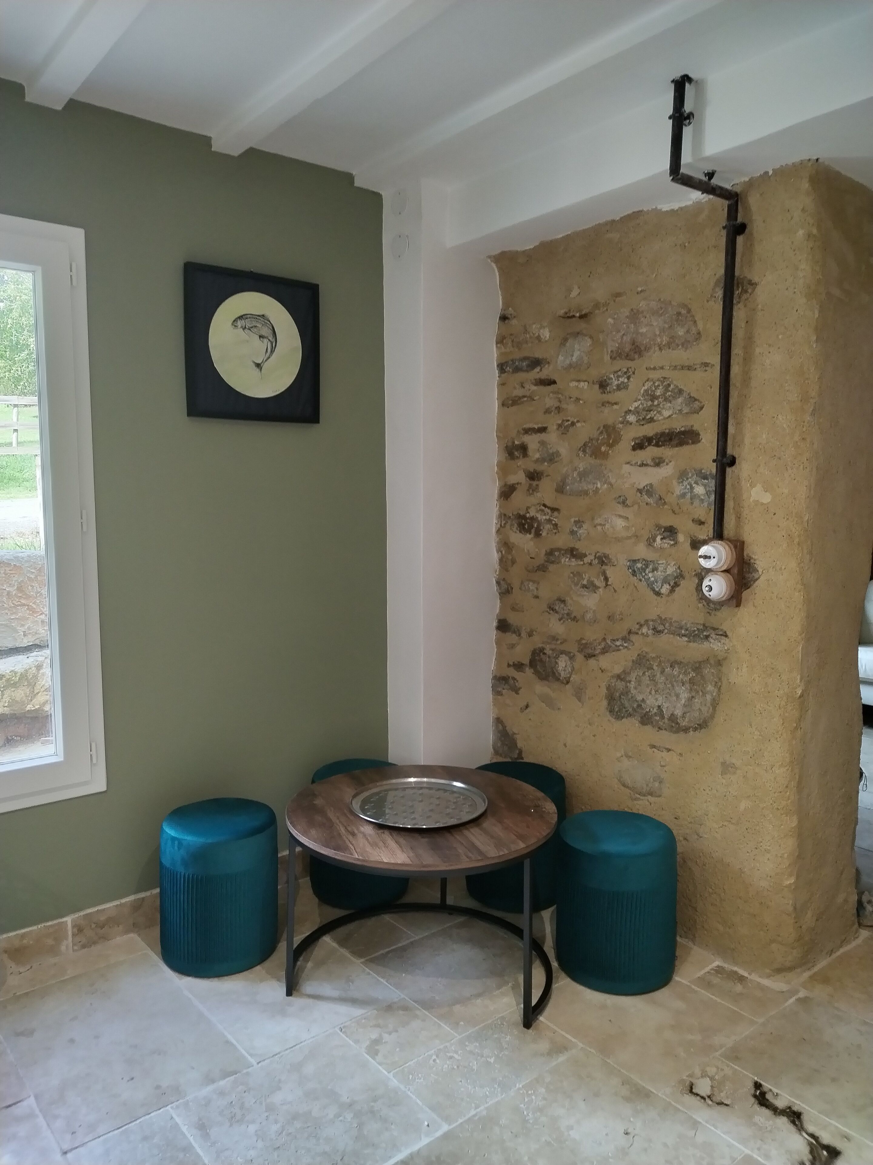 A room with a stone wall, a round table with a metal tray, and two blue stools.