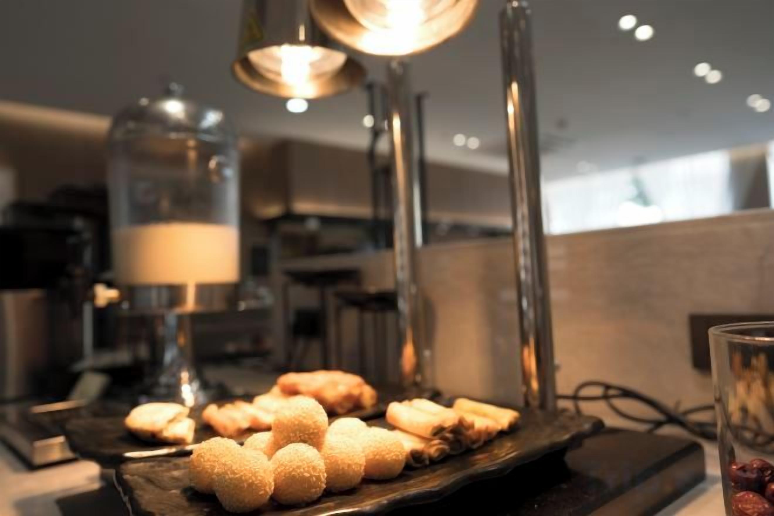 A dessert display with spherical treats on a wooden board, a glass container with a red object, and a lamp in the background.
