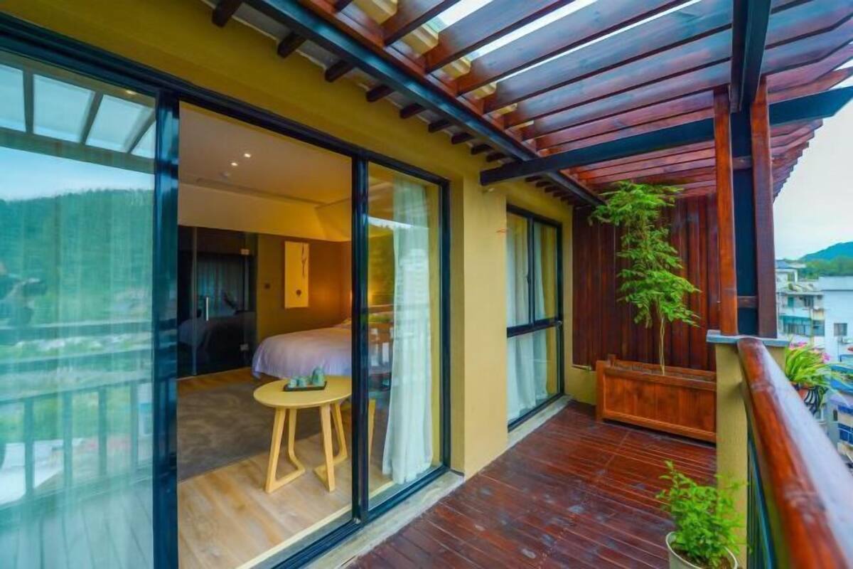 Une chambre d’hôtel moderne avec de grandes fenêtres, un balcon en bois et une vue sur l’extérieur.