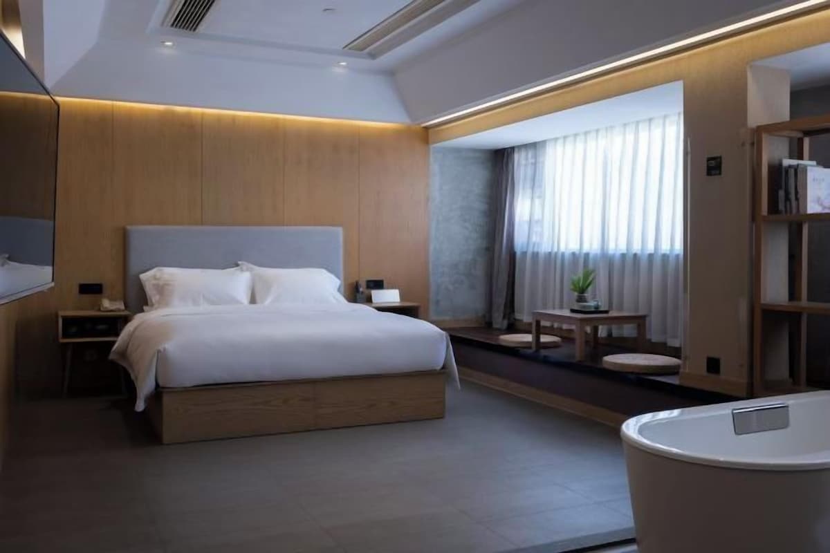 A modern hotel room with a large bed, bedside tables, a small seating area, and a bathroom.