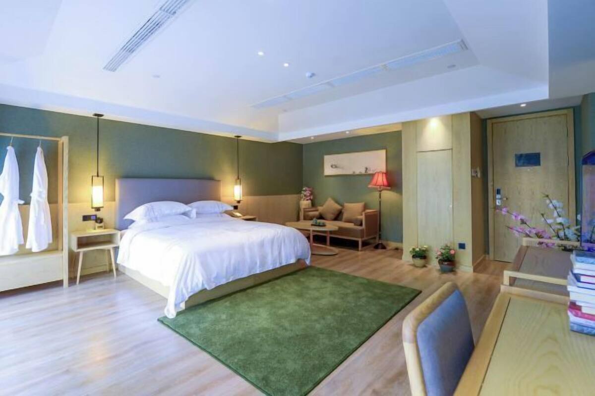 Une chambre d’hôtel moderne avec un lit, une table de chevet, une lampe et un tapis vert.