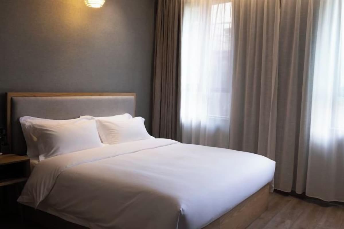 A hotel room with a large bed, a nightstand, and a wall-mounted light.