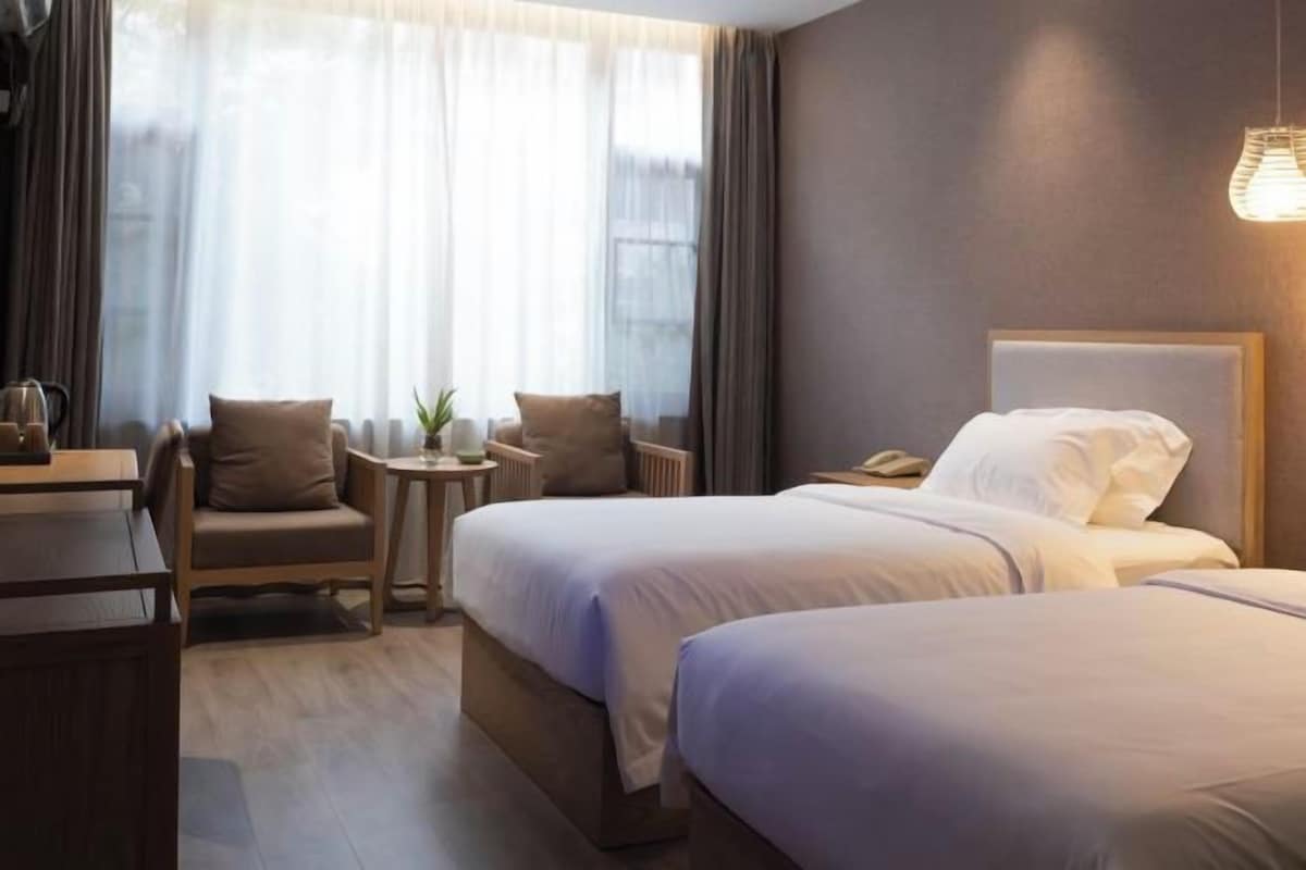 A hotel room with two beds, a desk, a chair, and a small table with a plant.