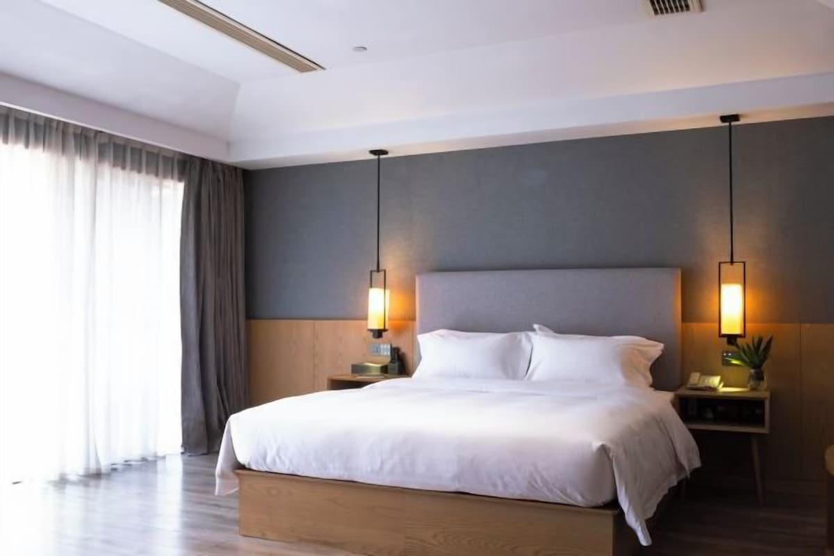 A modern hotel room with a large bed, bedside tables, and a view of the outdoors.