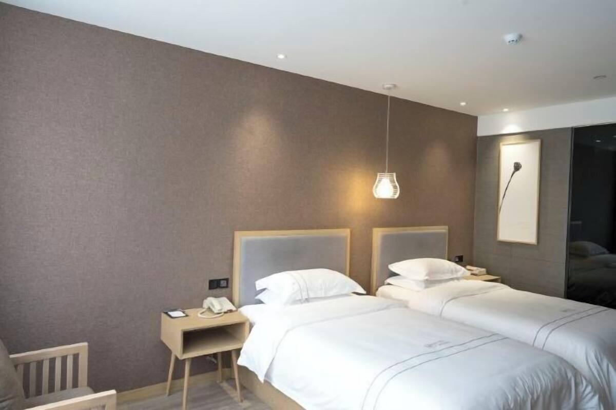 Une chambre d’hôtel avec deux lits, un bureau avec un téléphone et un luminaire suspendu.