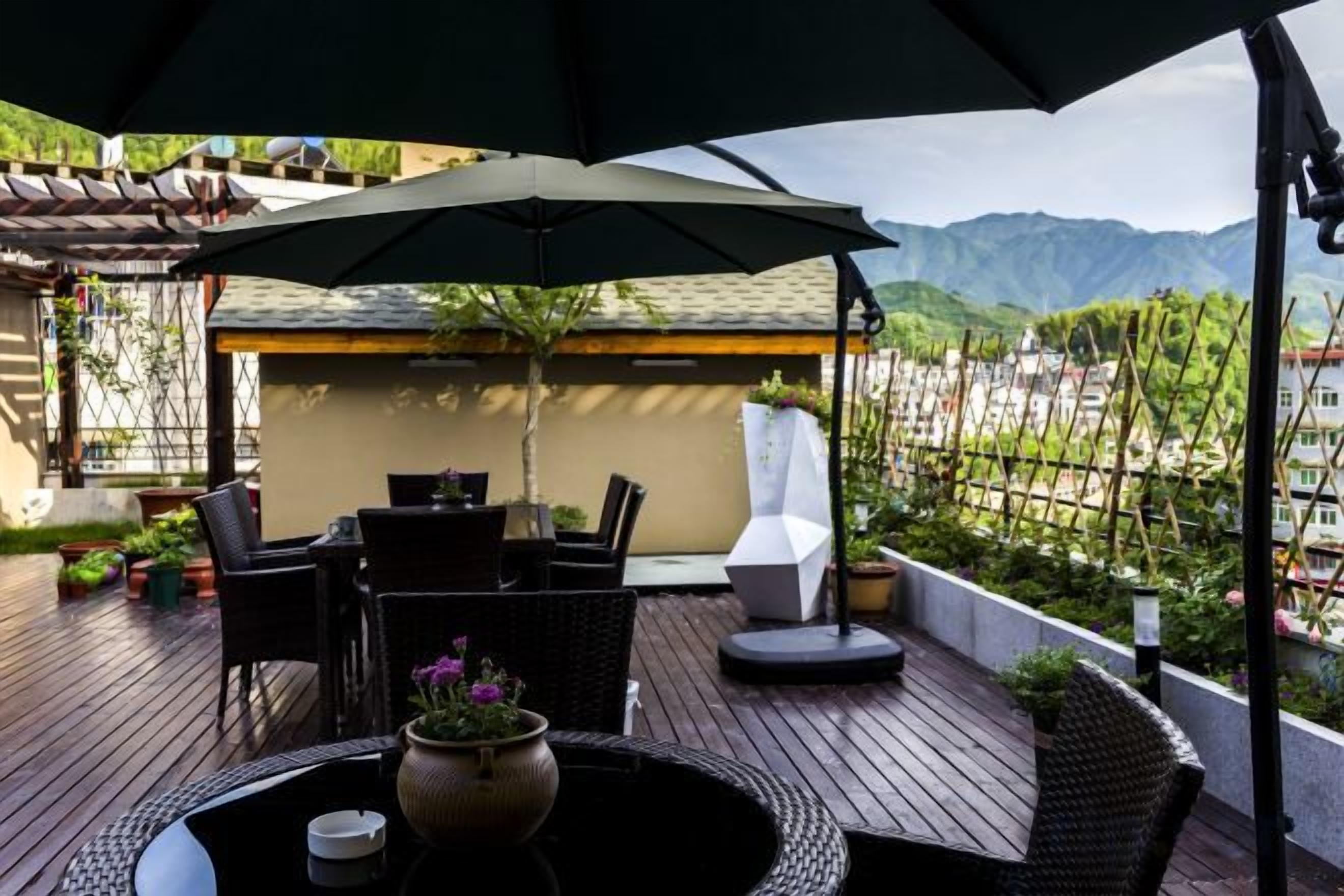 An outdoor patio with a table and chairs under an umbrella, overlooking a mountainous landscape.