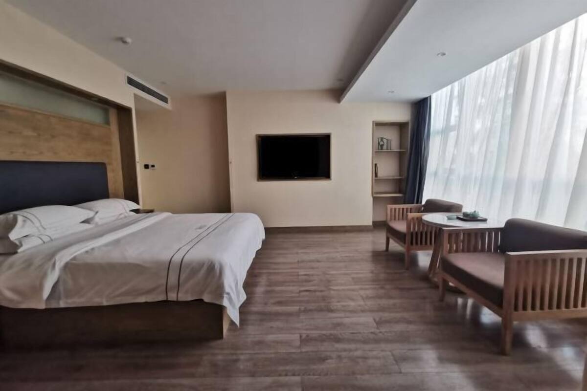Une chambre d’hôtel comprenant un lit, une télévision, un coin repas avec des chaises et une table, ainsi qu’une grande fenêtre avec des rideaux.