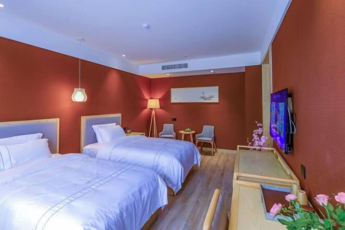 Une chambre d’hôtel avec deux lits, un bureau, une chaise, une télévision et une petite table agrémentée de fleurs.