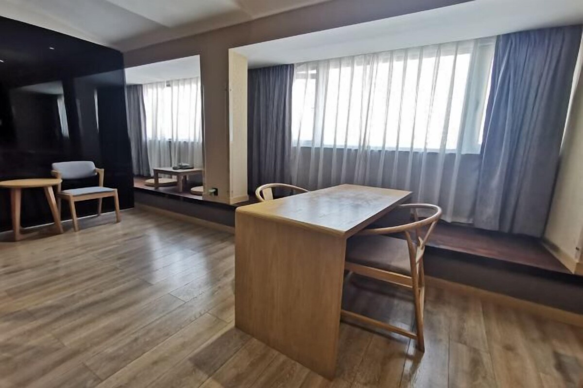 A modern hotel room with a wooden dining table, two chairs, a small side table, and a large mirror.