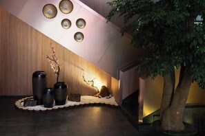 A reception area with a wooden wall, a reception desk, a large tree, and decorative vases. - Jiusu Culture Hotel (Suichang)