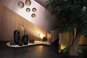 Un área de recepción con pared de madera, mostrador de recepción, un árbol grande y jarrones decorativos.