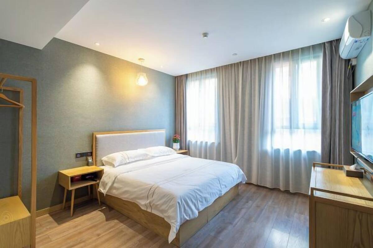 Une chambre d’hôtel moderne avec un grand lit, des tables de chevet, une télévision et une fenêtre avec des rideaux.