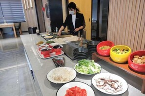 A buffet setup with various food items and a person serving. - Jiusu Culture Hotel (Suichang)