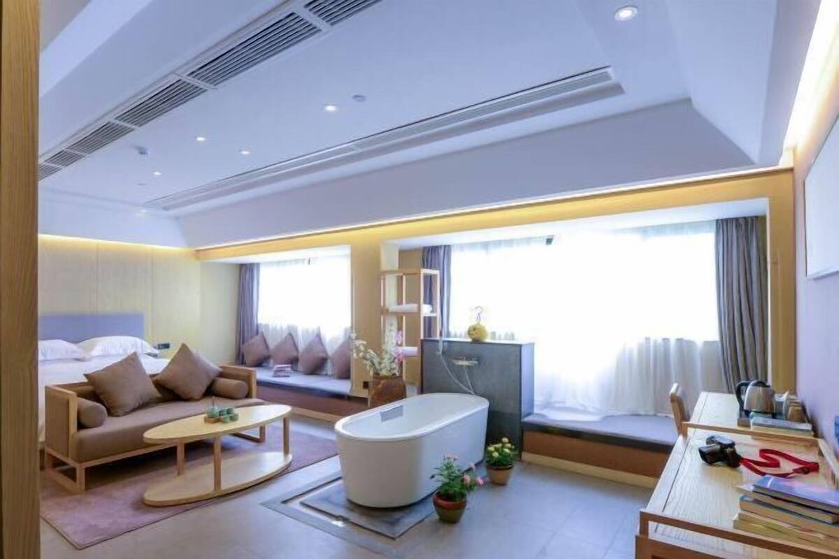 Une chambre d’hôtel moderne équipée d’un lit, d’un canapé, d’une table basse, d’une baignoire et d’un bureau avec des livres et une bouilloire.