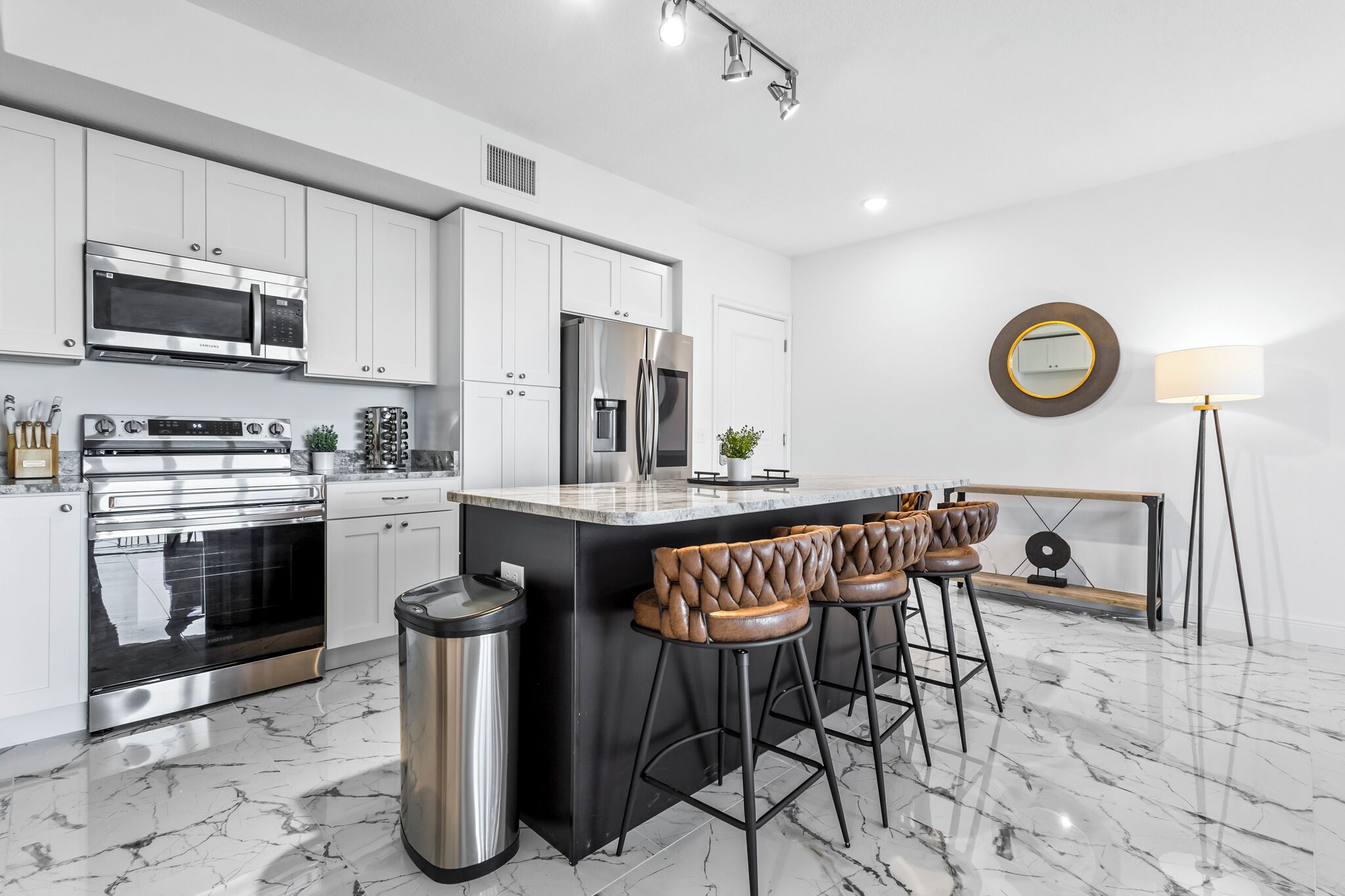 A modern kitchen with white cabinets, stainless steel appliances, a marble countertop, and a bar area with stools.