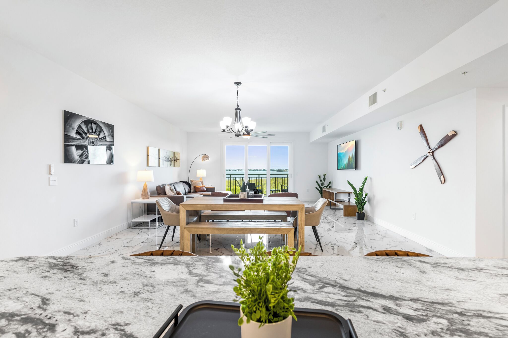 A spacious living area with a dining table, a chandelier, and a large window.