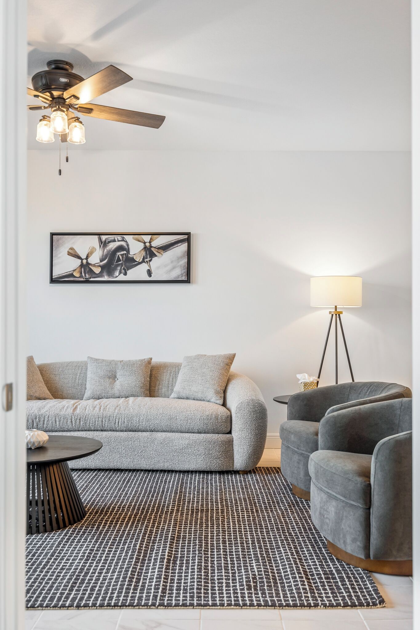 A modern living room with a gray sofa, a patterned rug, a standing lamp, and a ceiling fan.