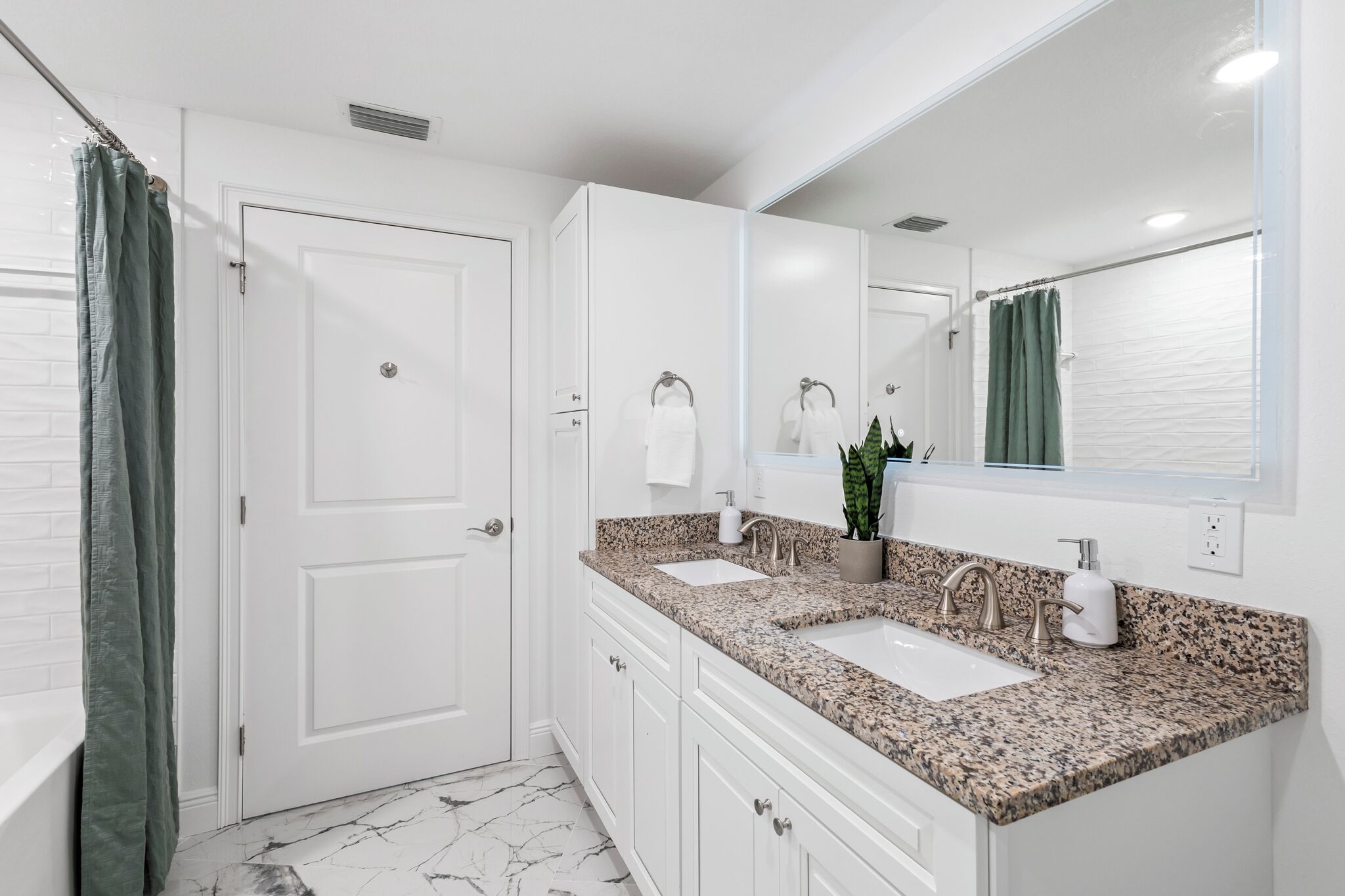 A modern bathroom with white cabinetry, a granite countertop, a double sink, a large mirror, and a shower curtain.