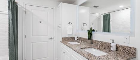 A modern bathroom with white cabinetry, a granite countertop, a double sink, a large mirror, and a shower curtain.